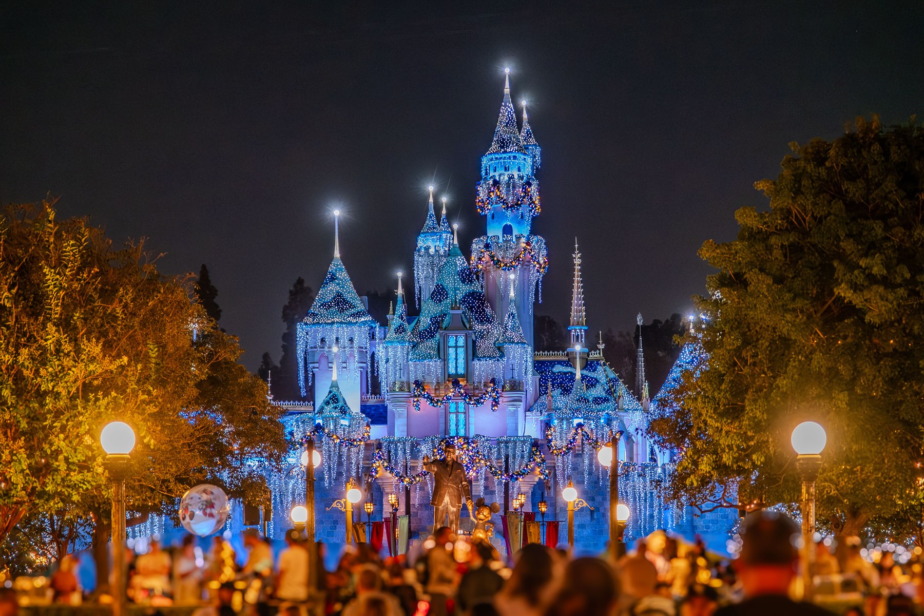 A brightly lit castle rises above an evening crowd.